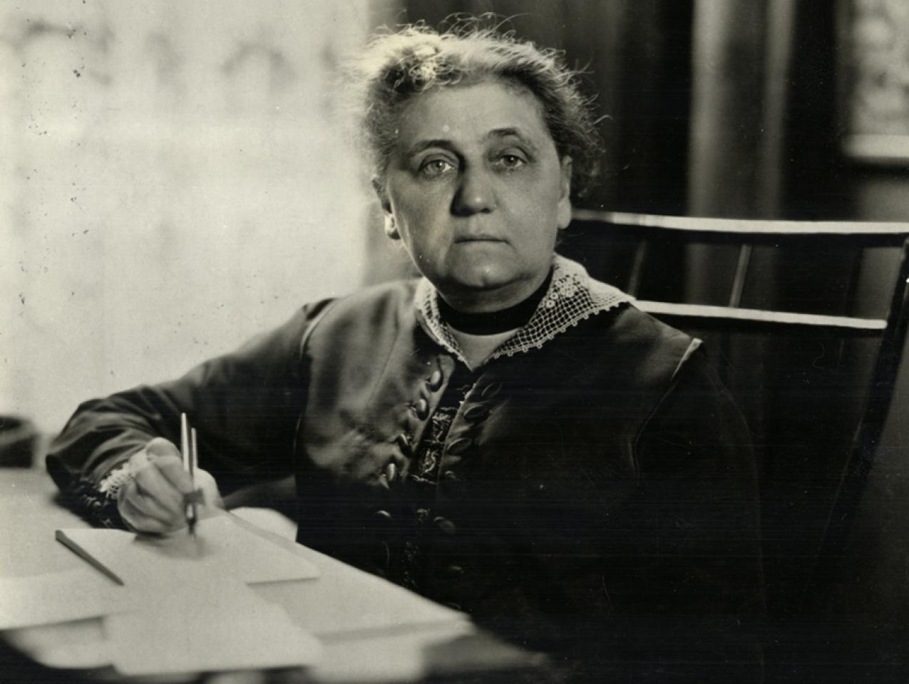 Portrait of Jane Addams sitting at her writing desk with pen in hand